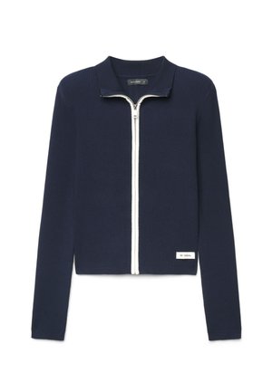 Giacca a maglia coste blu navy maniche lunghe con cerniera frontale bianca e piccola etichetta bianca vicino all'orlo con scritto "BE CASUAL."