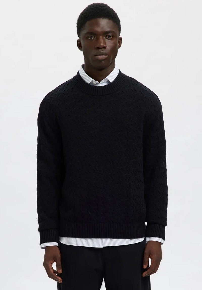 Suéter de punto azul marino con un patrón texturizado, cuello redondo y puños acanalados, combinado con una camisa de rayas blanca y azul.