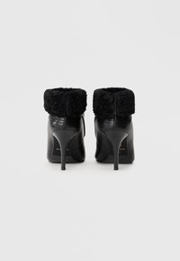 Botas de tobillo de cuero negro con un aterciopelado puño de piel de pelo negro, punta afilada y tacón de aguja delgado, con una cremallera en la parte trasera.