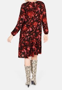 Robe à motif floral avec des manches longues, fond noir, fleurs rouges et roses. Accompagnée de bottes genoux en serpentin avec un bout pointu.