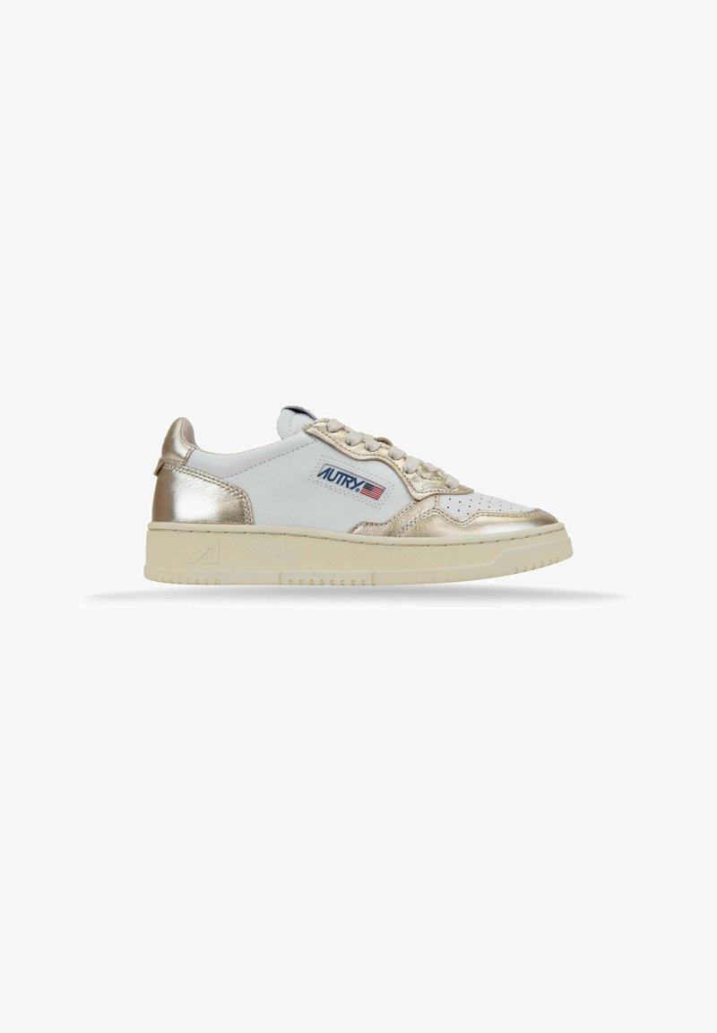 Sneaker in pelle bianca con accenti dorati metallici, punta perforata e suola in gomma color crema. Presenta un dettaglio del logo sul lato.
