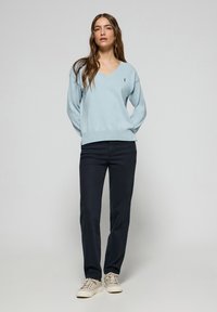 Pull en v bleu clair, en matériau doux, coupe décontractée. Associé à un pantalon bleu marine et des baskets beiges, créant un look décontracté.