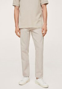 Pantalones de mezcla de algodón ligeros en beige con un corte recto, combinados con zapatillas blancas de caña baja, sobre un fondo neutro.