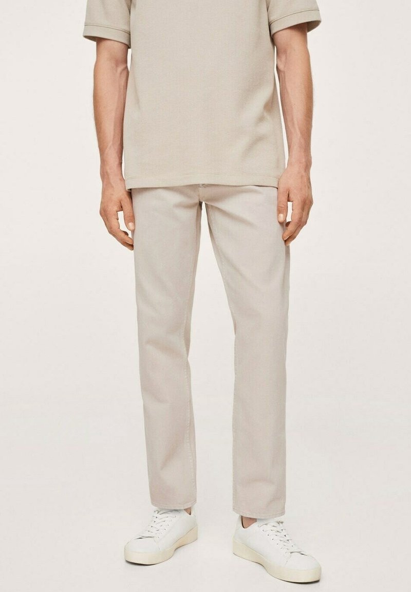 Pantalones de mezcla de algodón ligeros en beige con un corte recto, combinados con zapatillas blancas de caña baja, sobre un fondo neutro.