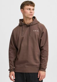 Hoodie marron en mélange de coton avec une coupe décontractée, doté de cordons de serrage et d'un logo en texte blanc "A.R.C." sur la poitrine.