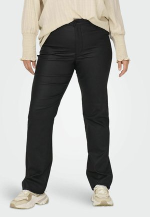 Schwarze, eng anliegende Hosen mit einer glatten Textur und einem subtilen Glanz. Kombiniert mit einem lockeren, hellen Oberteil und Sportschuhen.
