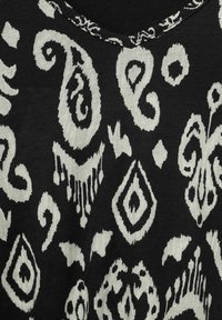 Tela negra con patrones abstractos de paisley y geométricos en blanco. Presenta un escote redondeado con acabado texturizado.