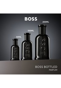 Drei schwarze BOSS Parfümflaschen in den Größen 50 ml, 100 ml und 200 ml vor einem grauen Farbverlauf-Hintergrund angezeigt.