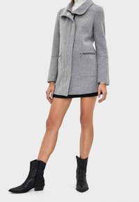 Grå ullkappa med stor krage, framdragkedja och två sidofickor med dragkedja, tillsammans med svarta läderankelboots.