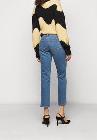 Jeans de mezclilla azul de cintura alta con pierna recta, combinados con un suéter de felpa con diseño negro y amarillo y tacones de aguja negros.