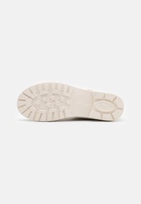 Suela de zapato de goma blanca con un patrón texturizado, que presenta surcos y formas de estrella. Detalle de logo circular cerca del talón.