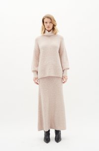 Maglione rosa accogliente con collo alto e maniche a caduta abbinato a una gonna maxi. Tessuto morbido e testurizzato, completato da stivali neri a punta.