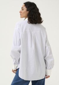 Hvid og lyseblå stribet skjorte med lange ærmer, oversized pasform, knaplukning ved håndleddene og rundet kant. Blødt stof, minimalistisk design.