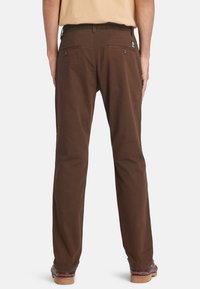 Pantaloni in cotone marrone con vestibilità rilassata, tasche standard e un'etichetta con logo sulla parte posteriore della vita. Design con frontale piatto e gamba dritta.