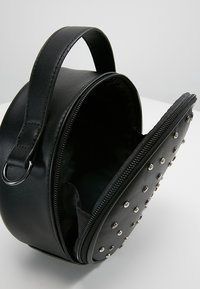 Round black faux leather bag with a zip closure and metal studded accents on one side. Includes a top handle for carrying.