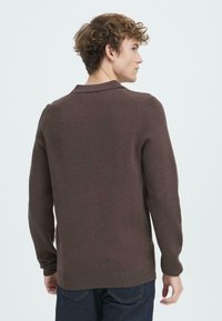 Pulover maro din tricot cu textură în dungi, având guler și mâneci lungi. Purtați-l cu blugi negri. Vedere din spate.