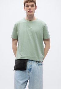 Light green cotton t-shirt with short sleeves and subtle "BOSS" logo. Worn with light blue denim jeans featuring a black leather pouch attached.