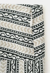 Tissu à motifs noirs, beiges et blancs avec des dessins géométriques et semblables à des vignes, doté d'un curseur de fermeture éclair blanc sur le bord.