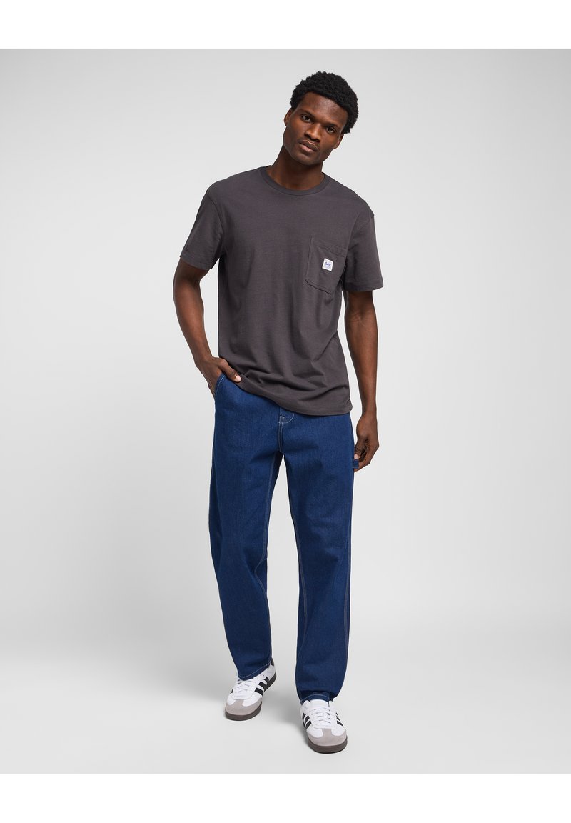 Dark gray short-sleeve t-shirt with a front pocket; paired with wide-leg blue denim jeans and white sneakers with black stripes.