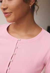 Ružový rebrovaný top s okrúhlym výstrihom a striebornými gombíkmi vpredu, so hladkou textúrou a priliehavým strihom.