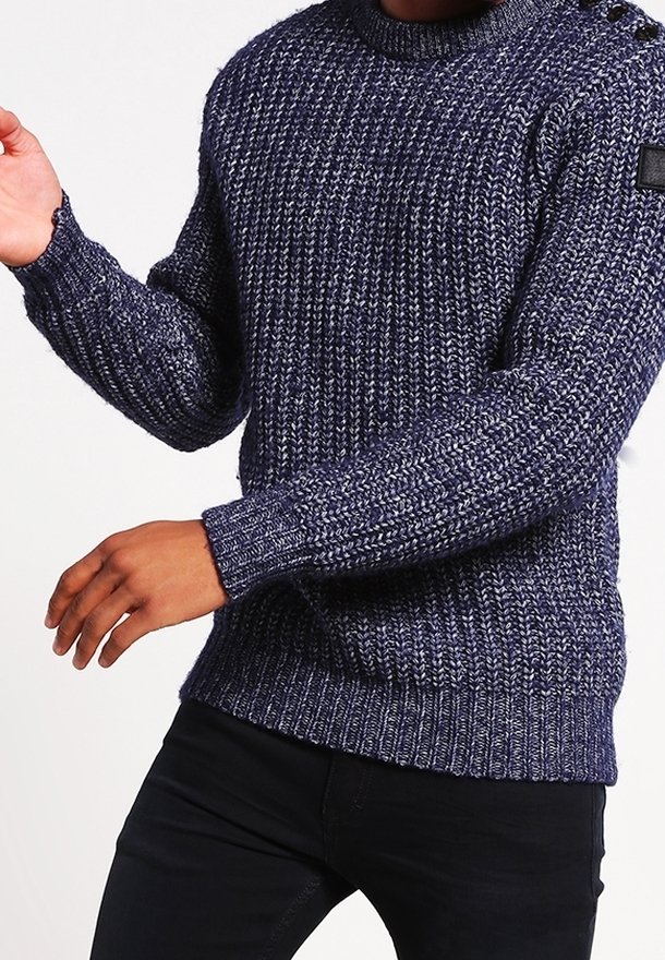 Navyblå stickad tröja med en strukturerad mönstring, långa ärmar och ribbade muddar. Har en rund halsringning och knappar på axeln.