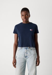 Mørkeblå crop t-shirt lavet af bomuld med rund hals, prydet med et lille logo i hvid, rød og blå på venstre bryst.