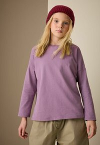 Purple long-sleeve t-shirt with a relaxed fit and round neckline, paired with light-colored, loose-fitting pants. Notable soft cotton texture.