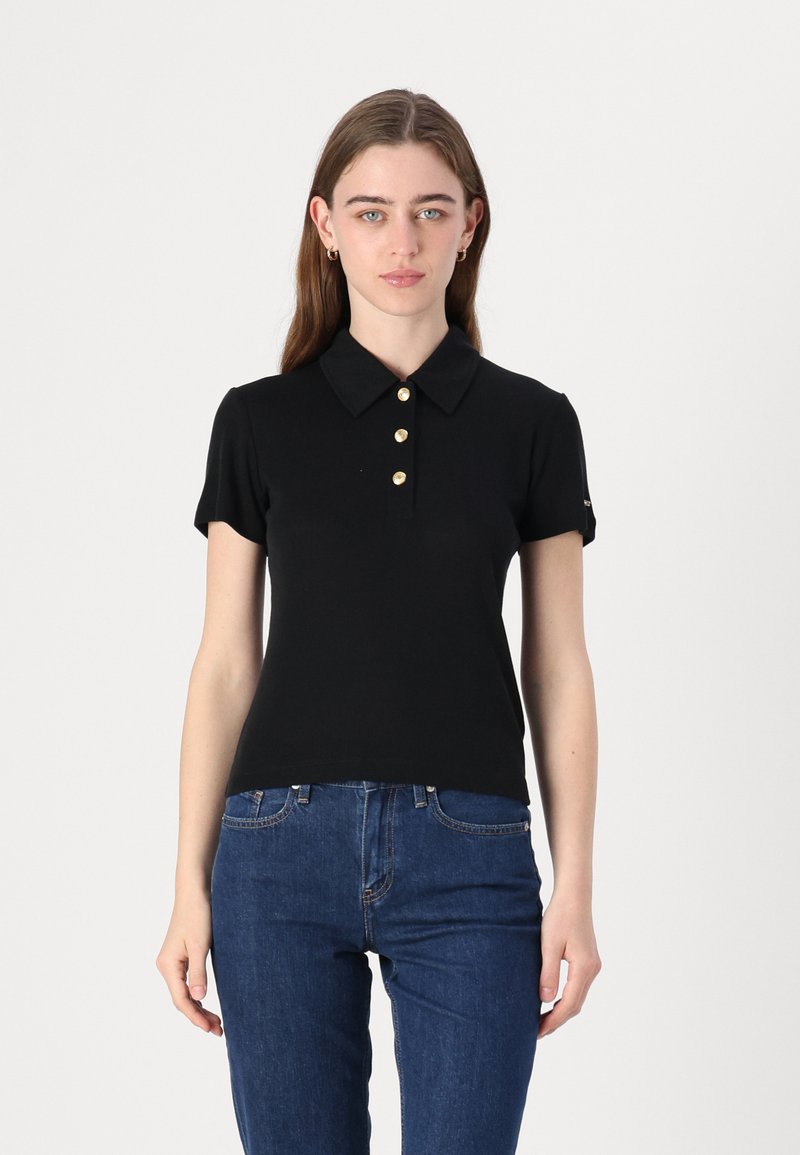 Svart kortermet polo skjorte med krage, med fire gullknapper i pløssen, tettsittende design og myk, glatt tekstur. Kombinert med blå jeans.