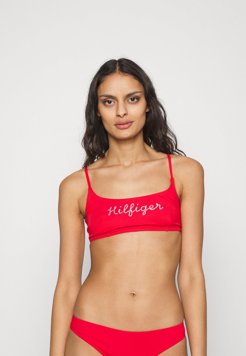 Top bikini rosso con spalline sottili, caratterizzato dalla scritta bianca "Hilfiger". Tessuto liscio e elasticizzato con un design aderente.