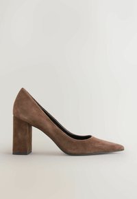 Escarpin en daim marron à bout pointu avec un talon bloc épais, présenté en profil latéral sur un fond clair uni.