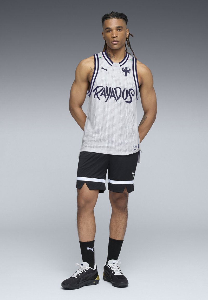 Hvid mesh basketballtrøje med "RAYADOS" tekst i blå, sammen med sorte shorts med hvide striber og sneakers.