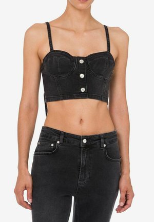 Donna che indossa un top bustier corto in denim nero con bottoni argentati e jeans in denim nero a vita alta, mostrata dal collo ai fianchi.