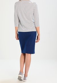 Randig långärmad topp i vitt och marinblått, kombinerad med en blå knälång kjol och grå sneakers, sedd bakifrån. Slät tyg.