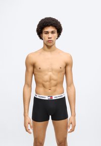 Μαύρα μπόξερ βρακάκια με λευκή μέση με σήμανση και κόκκινες και μπλε λεπτομέρειες, που φοριούνται από έναν άντρα μοντέλο με καλοσχηματισμένο σώμα.