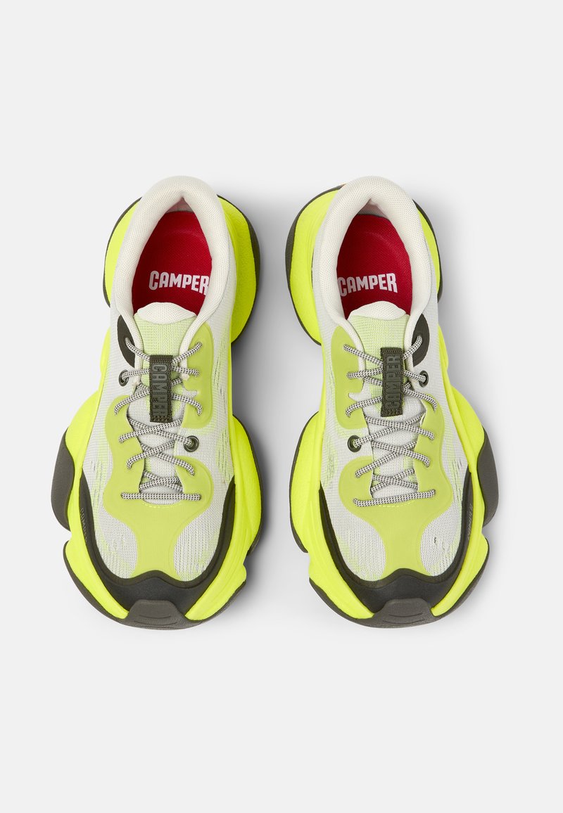 Ett par neongula och vita Camper-sneakers med grå detaljer och röda innersulor, sett ovanifrån på en vit bakgrund.