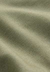Texturerat tyg i dämpad olivgrön. Mjuk, slät yta med en lätt lyster, med fina vävda mönster som skapar visuell djup.