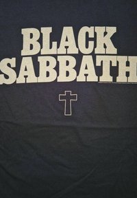Černé tričko s výrazným textem v světlých barvách, který zní "BLACK SABBATH", pod nímž je malý design kříže. Hladká struktura látky.