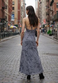 Sivé maxi kvetinové šaty s tenkými ramienkami, otvorenými chrbtom a prúdiacou siluetou, doplnené čiernymi členkovými topánkami na mestskom chodníku.