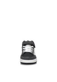 Scarpa sportiva nera e grigia con colletto imbottito, lacci bianchi e una cinghia con chiusura a strappo; presenta materiali lisci e testurizzati.