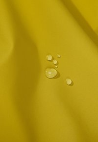 Tessuto giallo con una superficie liscia, caratterizzato da diverse gocce d'acqua di varie dimensioni che si posano sulla superficie.