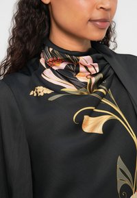 Căciulă neagră cu modele florale în nuanțe de roz deschis, auriu și roșu. Textură netedă cu un design drapat, evidențiind detalii intricate.