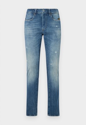 Niebieskie dżinsy o prostym kroju, z wyraźnie wyblakłą teksturą, efektem whiskering oraz przetarciami na kolanach. Klasyczny fason pięciu kieszeni.