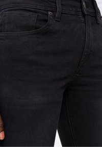 Svarta denimjeans har en slim fit-design, framträdande framfickor och en subtil textur, med en klassisk knapp- och dragkedjestängning.