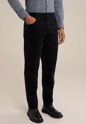 Pantaloni in corduroy neri con tasche laterali e taglio dritto. Abbinati a una camicia blu a trama e stivali in pelle neri.