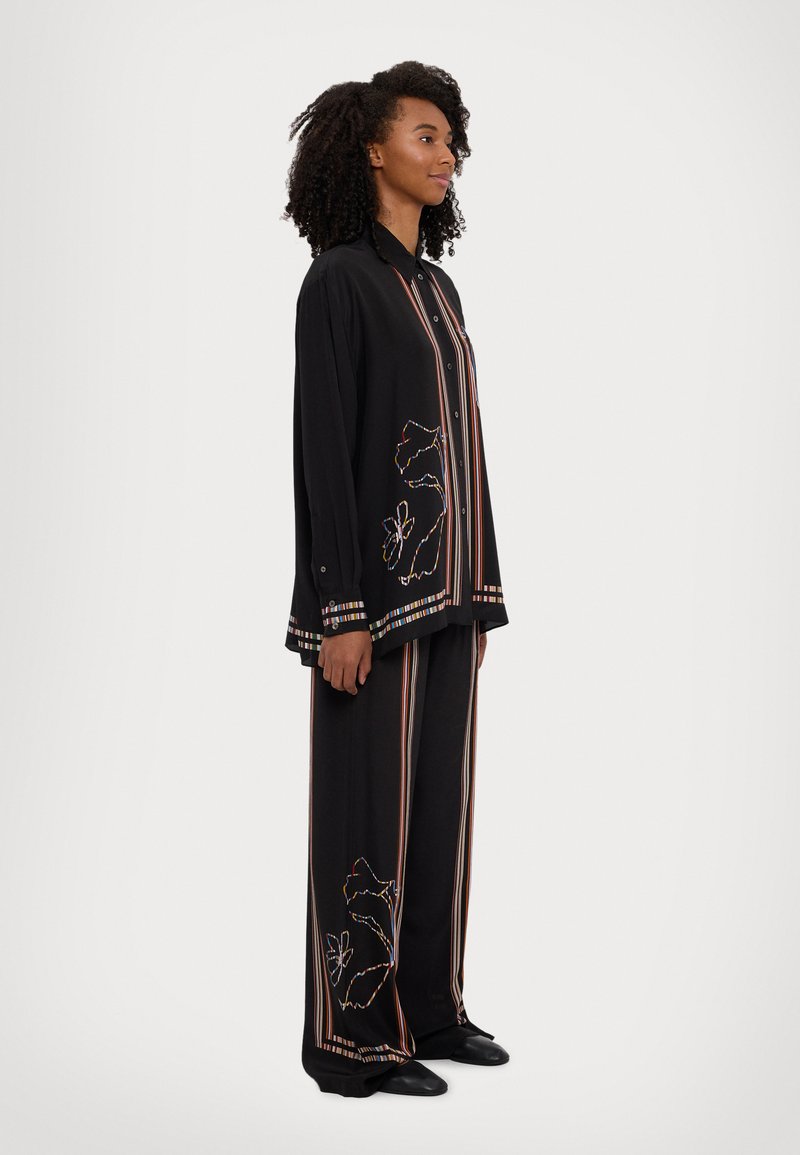 Black, loose-fitting shirt and pant set featuring colorful vertical stripes and floral embroidery. Fabric appears smooth with a slight sheen.