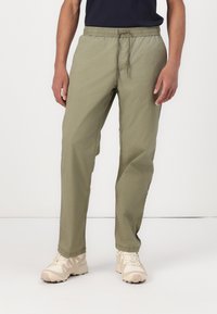 Lyse olivenfargede bukser med elastisk midje og snor. Ledig passform med sidelommer, laget av mykt stoff. Brukt med beige sneakers.