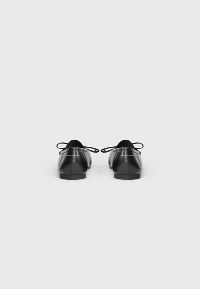 Ballerines en cuir noir avec un bout arrondi, un détail en lacet à l'arrière et une texture lisse. Design simple et minimaliste.