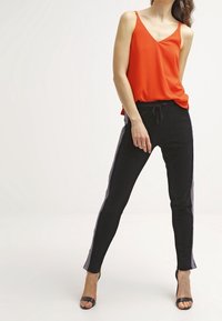 Top rojo sin mangas con escote en V combinado con pantalones negros ajustados que presentan rayas laterales blancas y moradas y una cintura elástica.