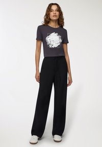 Czarne spodnie z szerokimi nogawkami w połączeniu z ciemnoszarym t-shirtem z białym abstrakcyjnym wzorem. Stylizację dopełniają białe sneakersy.