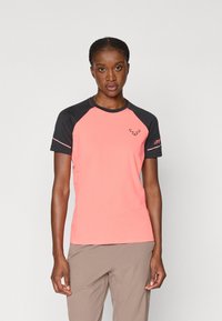 T-shirt de mangas curtas em coral brilhante com mangas raglan pretas; apresenta logotipo no peito e na manga; textura suave e corte atlético.